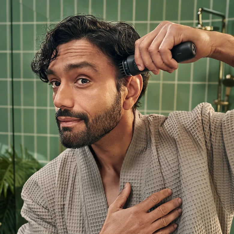 Man in a bathrobe grooming himself with a hairbrush in a bathroom.