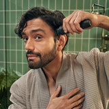 Man in a bathrobe grooming himself with a hairbrush in a bathroom.