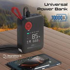 A black portable power bank with a red carrying loop and digital display, shown on a wooden table outdoors with a blurred forest background. A smartphone and tablet are charging from its USB-C port.